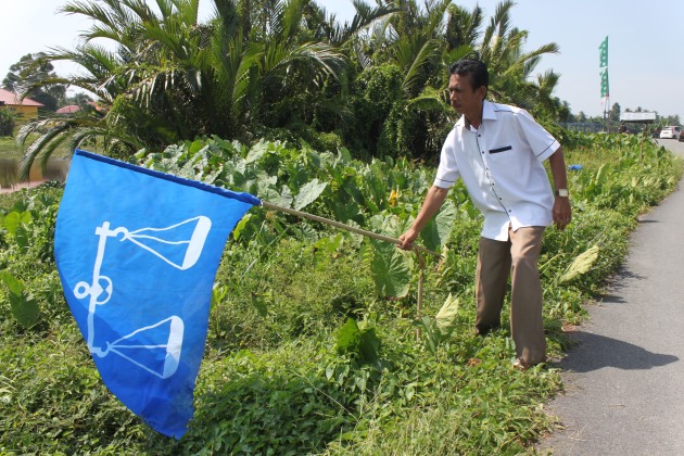Rosli Mohd. Noor menunjukkan sebahagian bendera Barisan Nasional yang dirosakkan di Kampung Kuau.